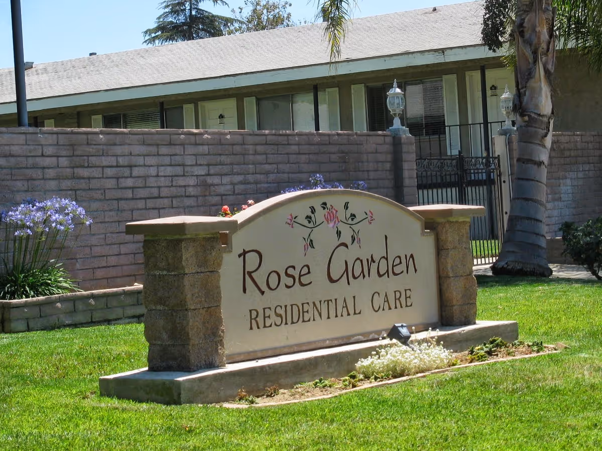 Stone sign reading Rose Garden Residential Care on a lawn in front of a brick building.