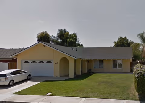 Single-story beige senior living home with attached garage, driveway, and manicured lawn.
