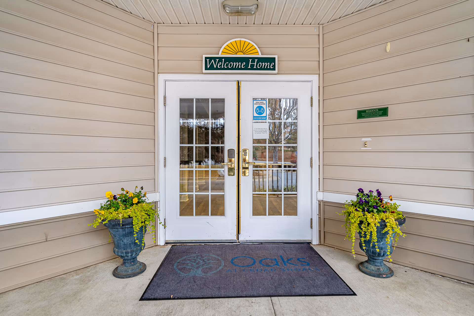 Double glass doors with a Welcome Home sign, planters, and a mat at the entrance.