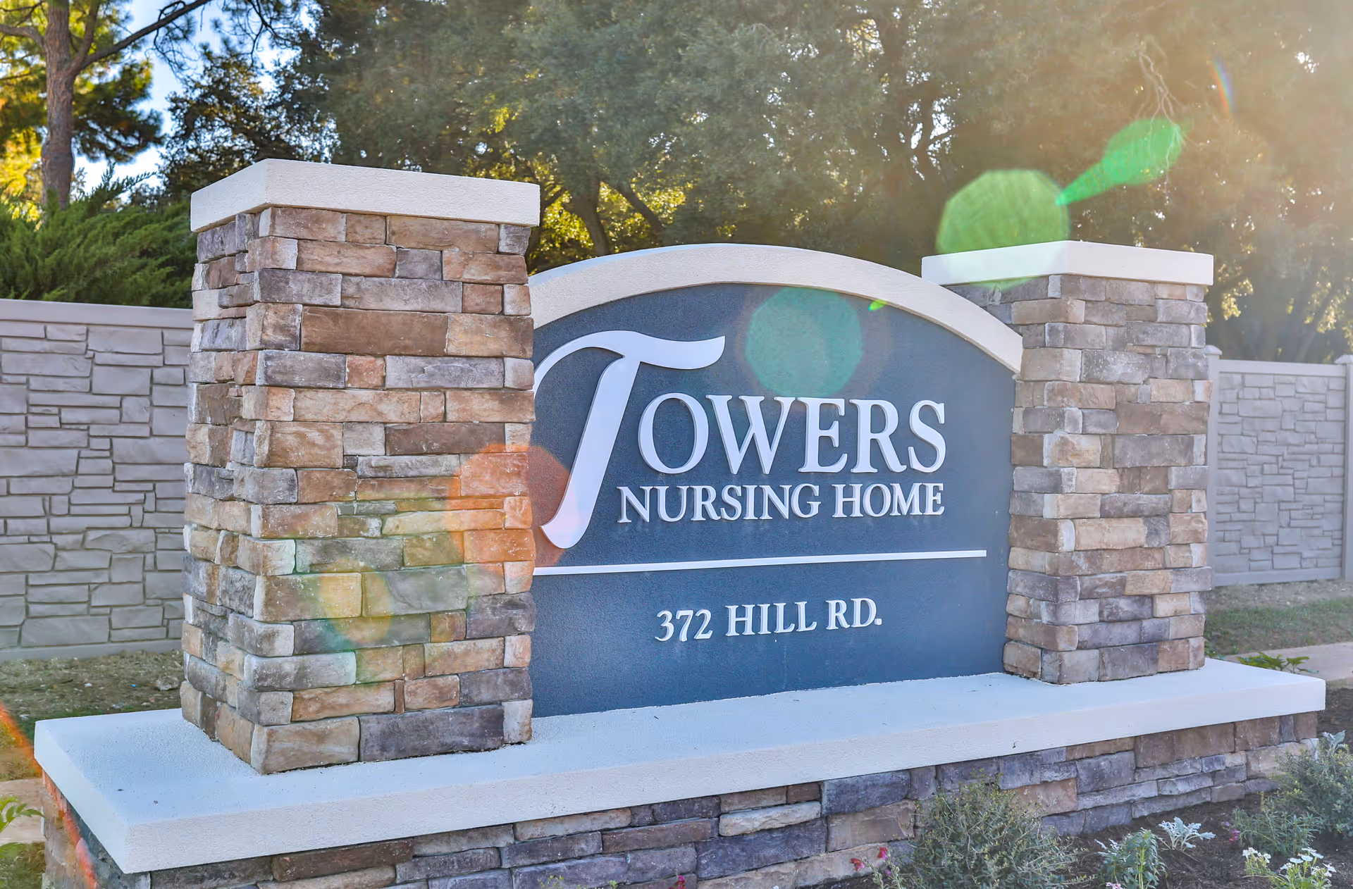 Entrance sign for Towers Nursing Home with stone pillars and landscaped surroundings.