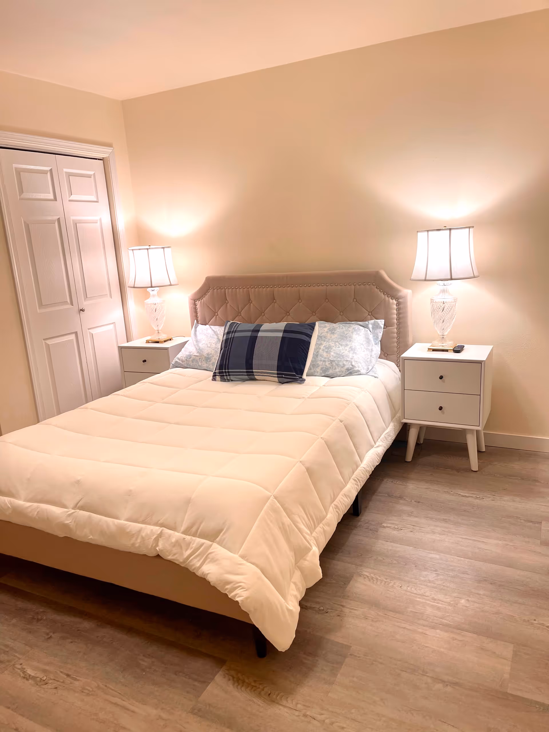 A neatly made bedroom with a tufted headboard, nightstands, lamps, and soft beige walls.