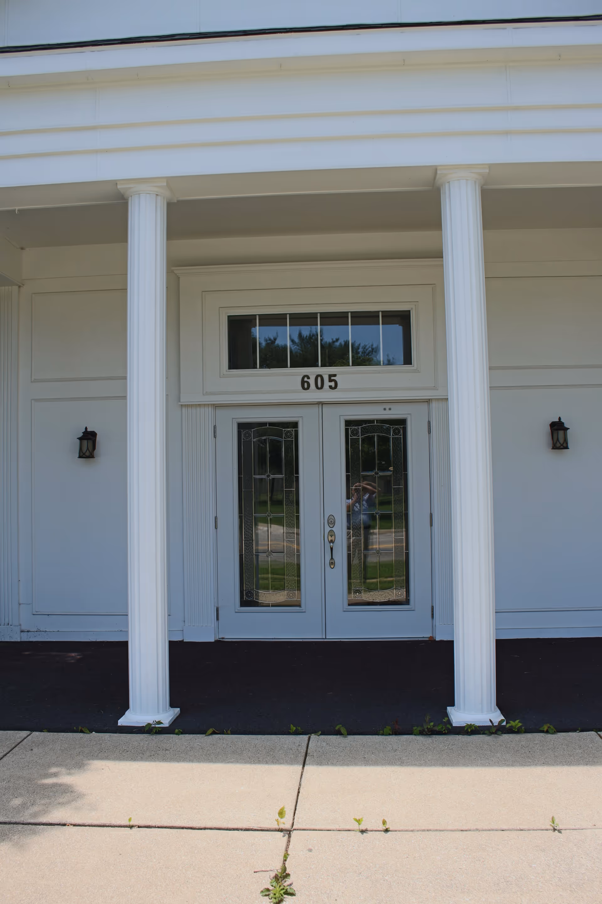 White building entrance with two columns, glass-paneled doors, and 605 above.