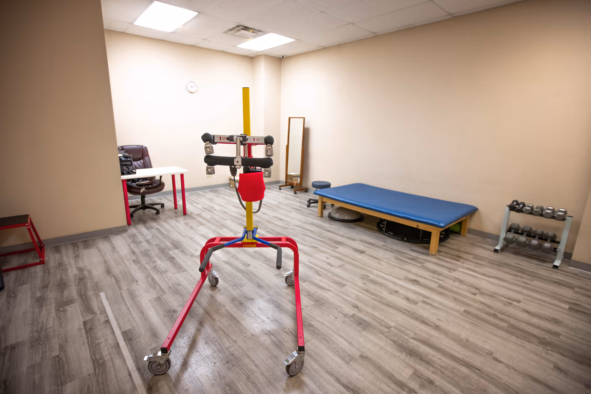 Interior rehab gym with exercise equipment, a blue bench, and weights.