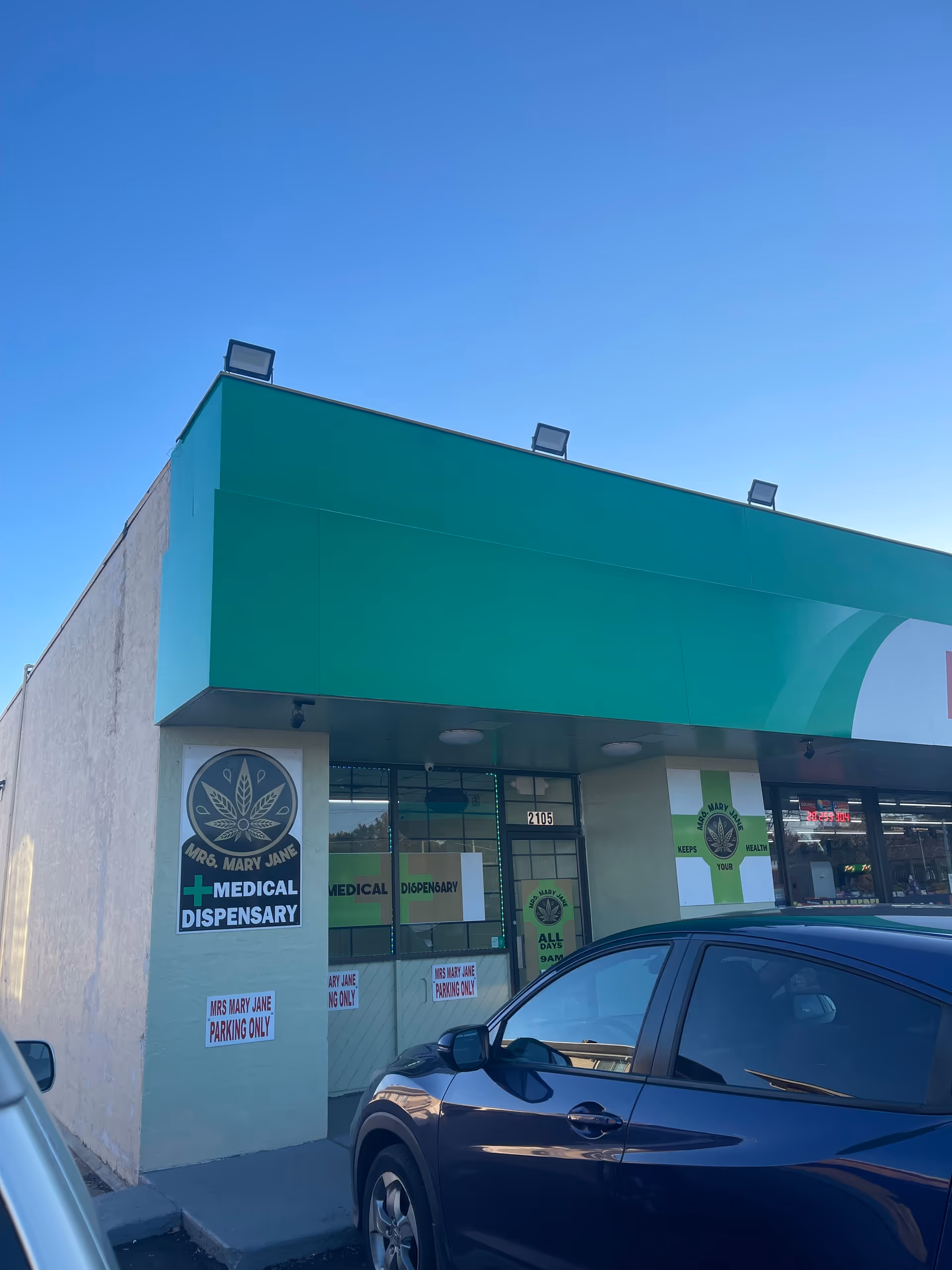 Exterior front of a green storefront labeled Mrs Mary Jane, medical dispensary, with parked car.