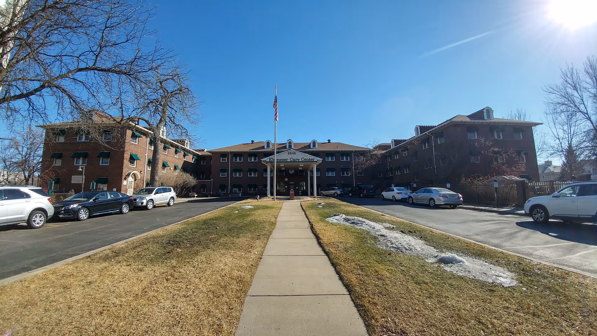 Exterior view of Ebenezer Care Center with walkway, flagpole, and parked cars.