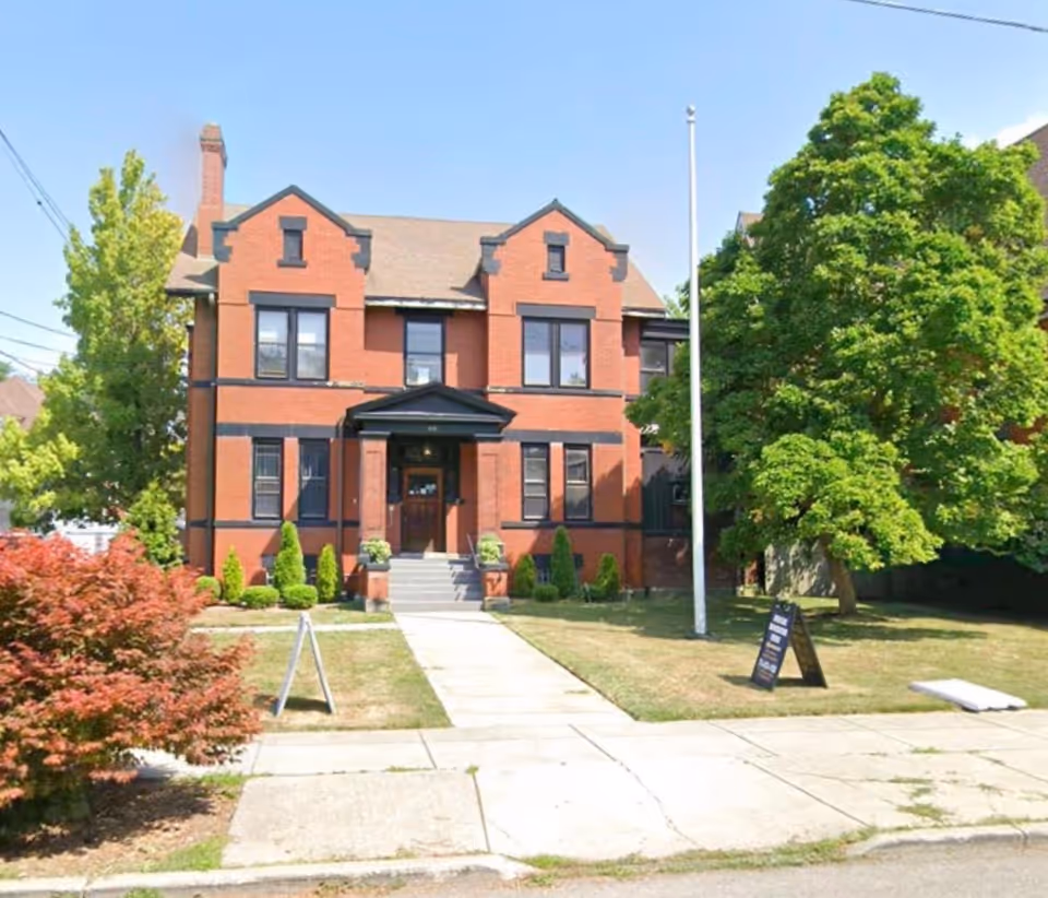 Red brick, multi-story building with steps and lush trees in front yard.