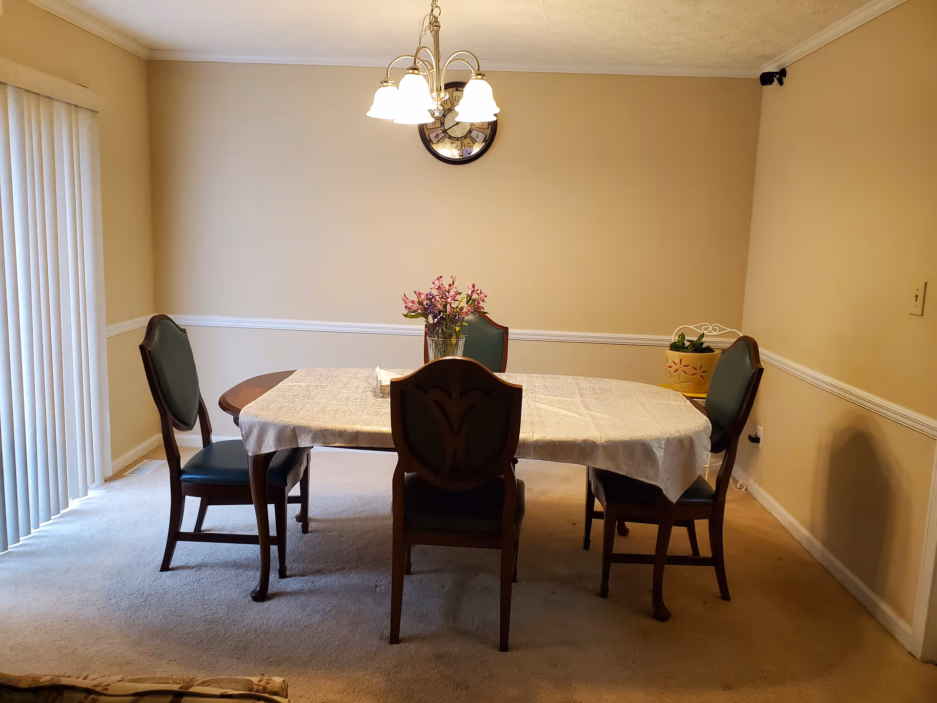Dining room with a four-seat table, chandelier, vase of flowers, and four chairs.