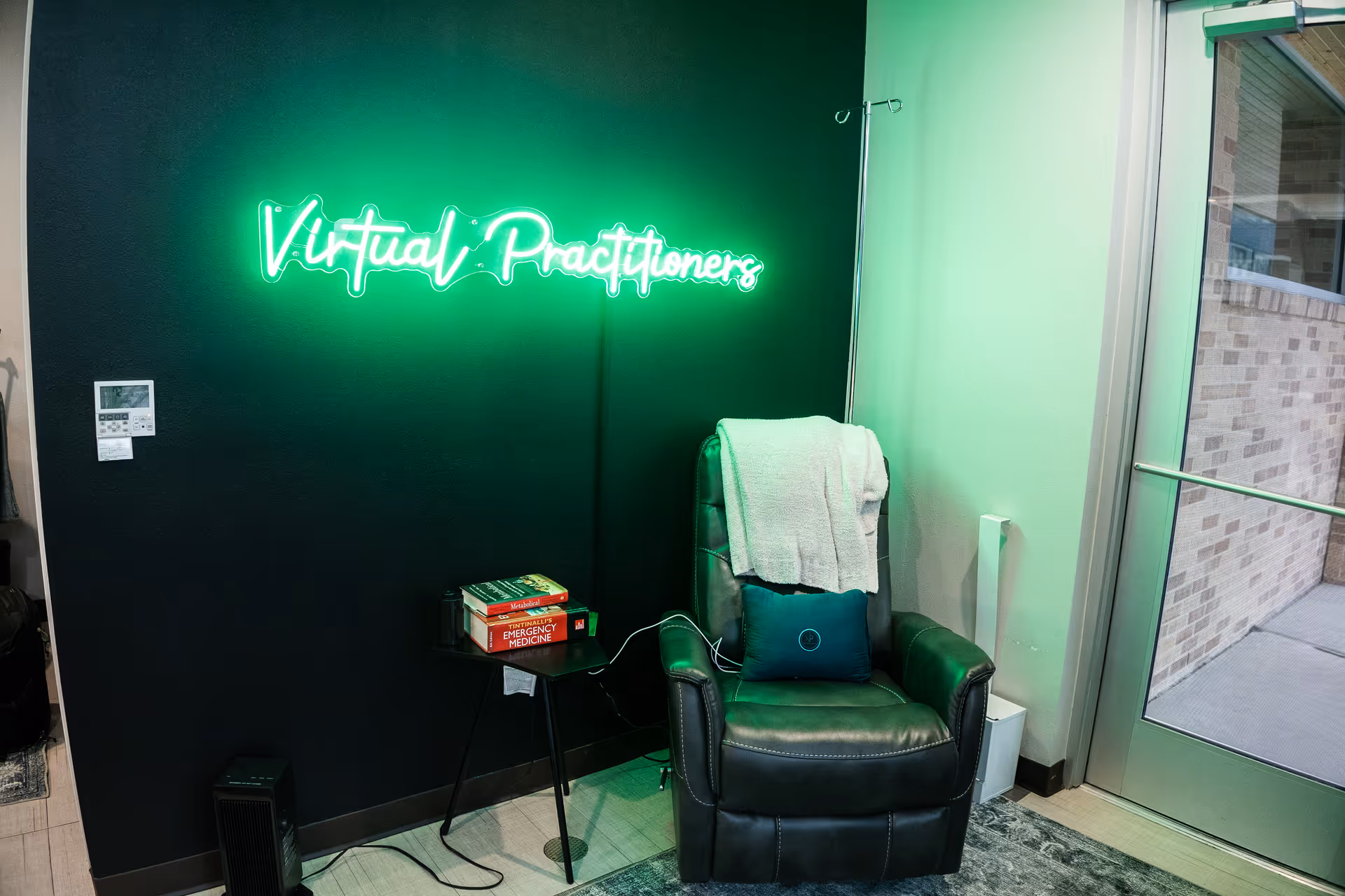 Neon green sign reading Virtual Practitioners on a dark wall beside a leather chair.