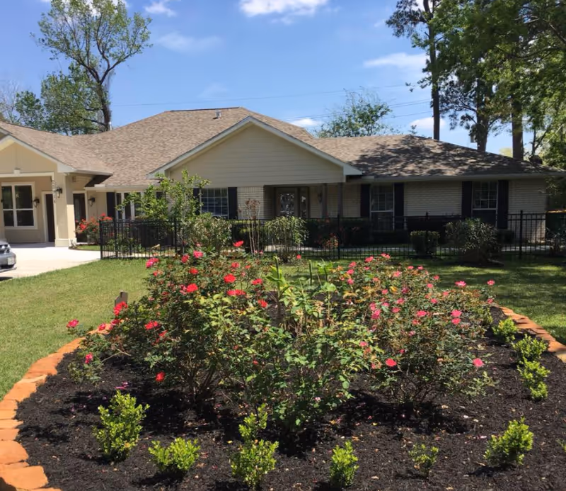 Single-story care home exterior with a front garden of rose bushes and a black fence.