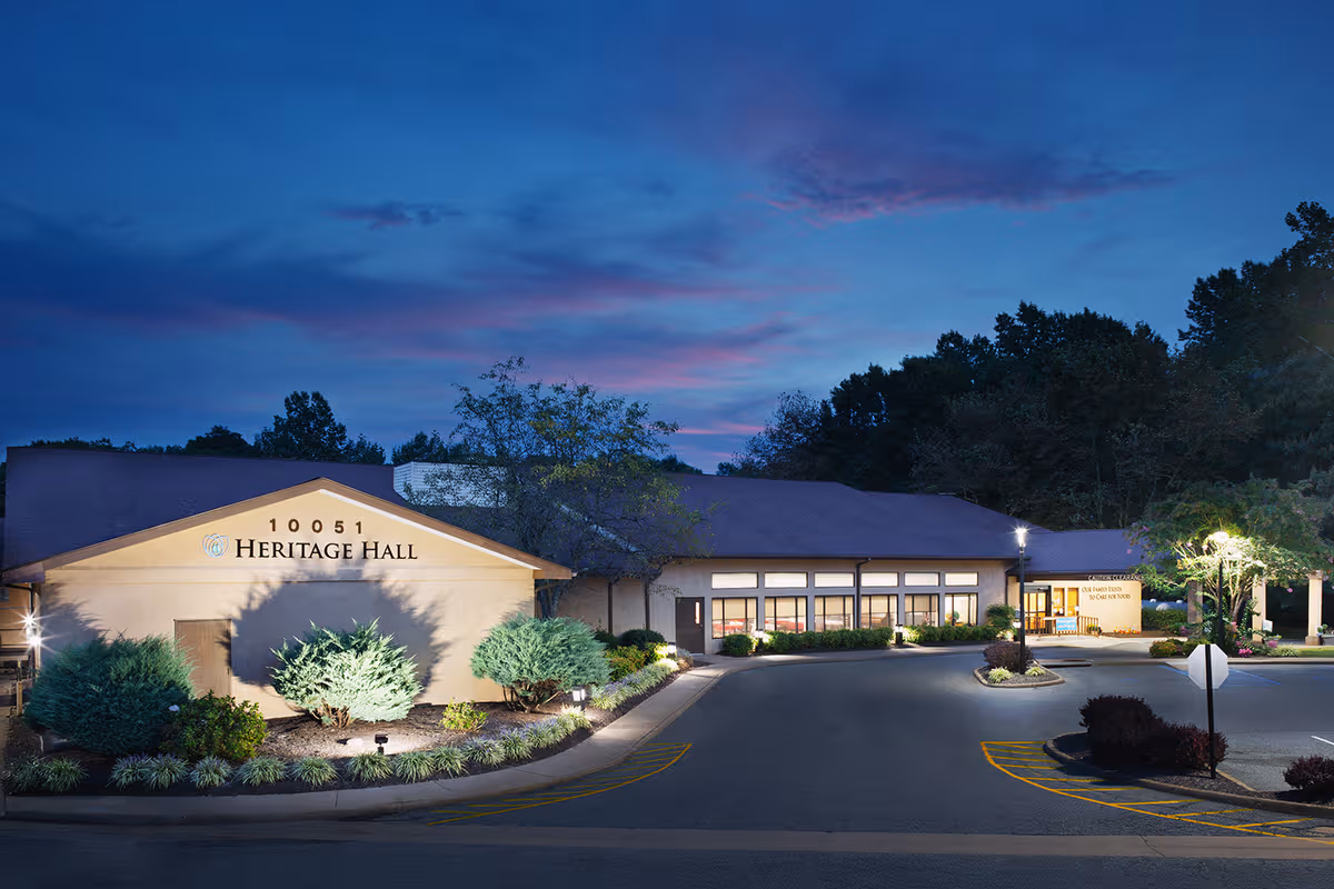 Evening exterior view of Heritage Hall King George with landscaped entrance and surrounding parking lot.