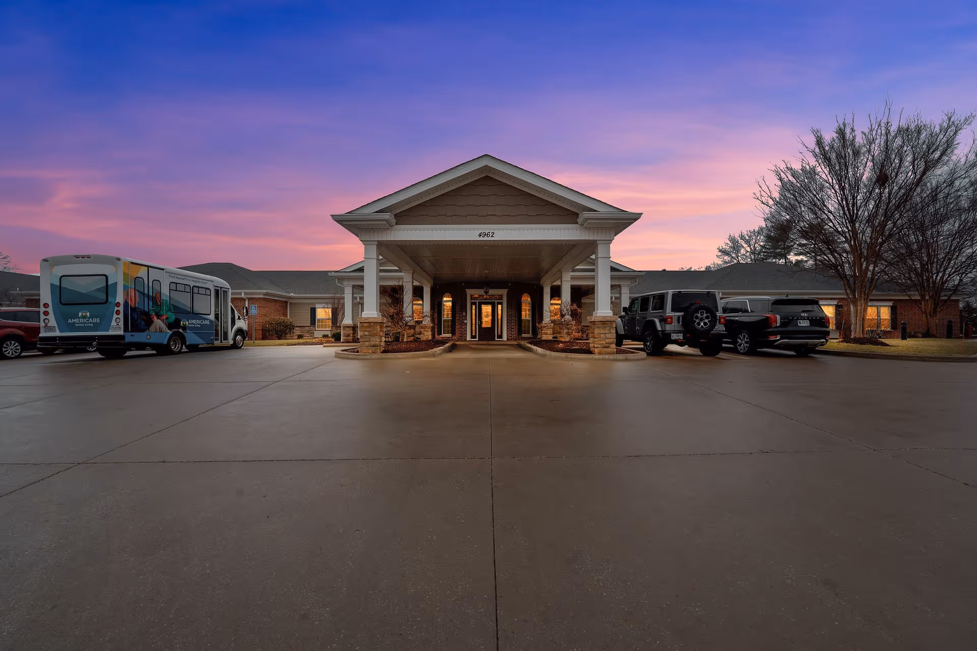 Front entrance of a senior living facility with a bus and parked cars.