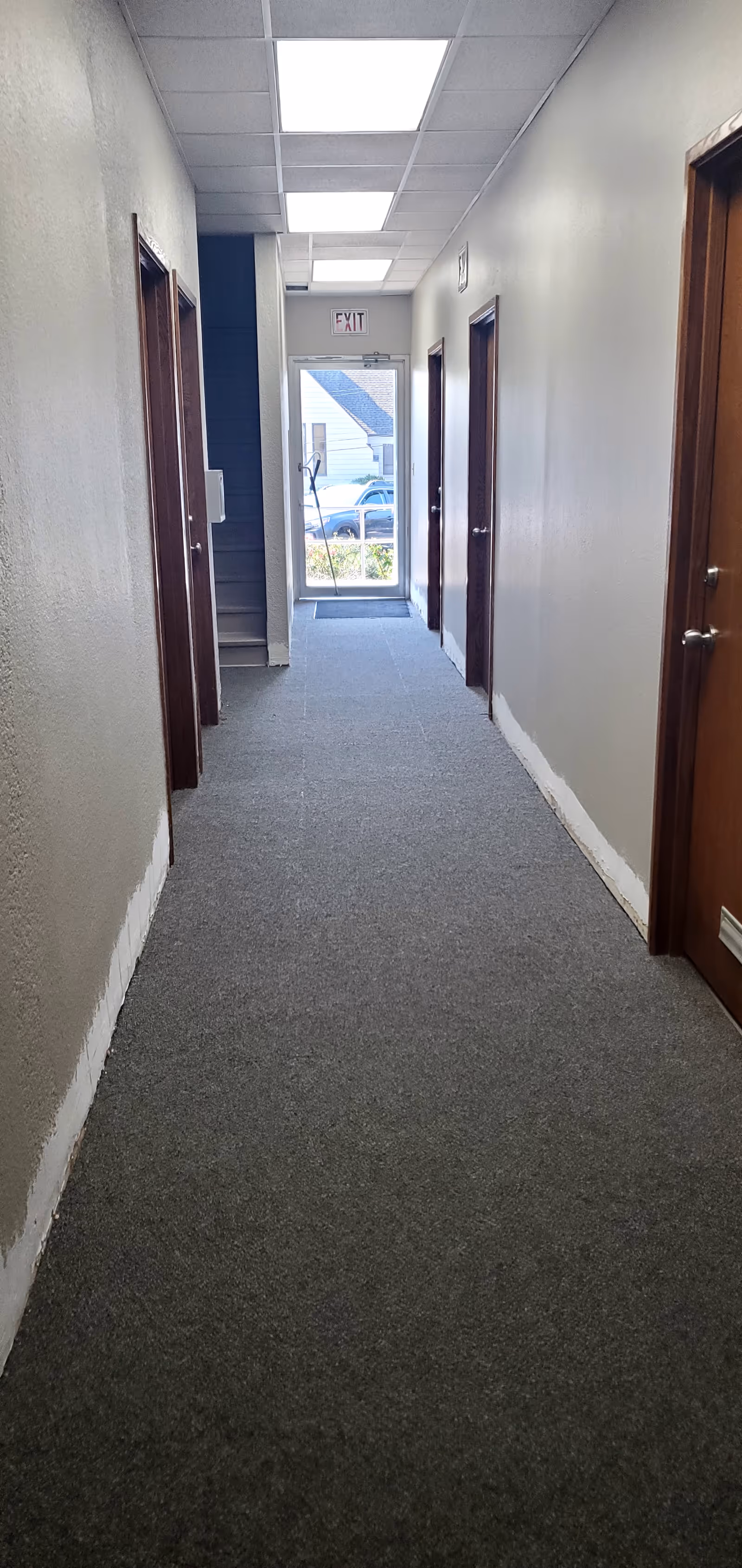 Long hallway inside a senior living facility with doors on both sides and an exit ahead.