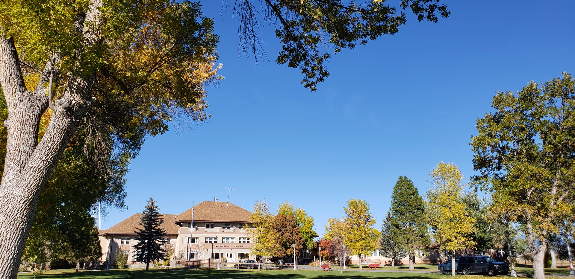 Front view of a large facility building with a brown roof, green lawn, and trees.