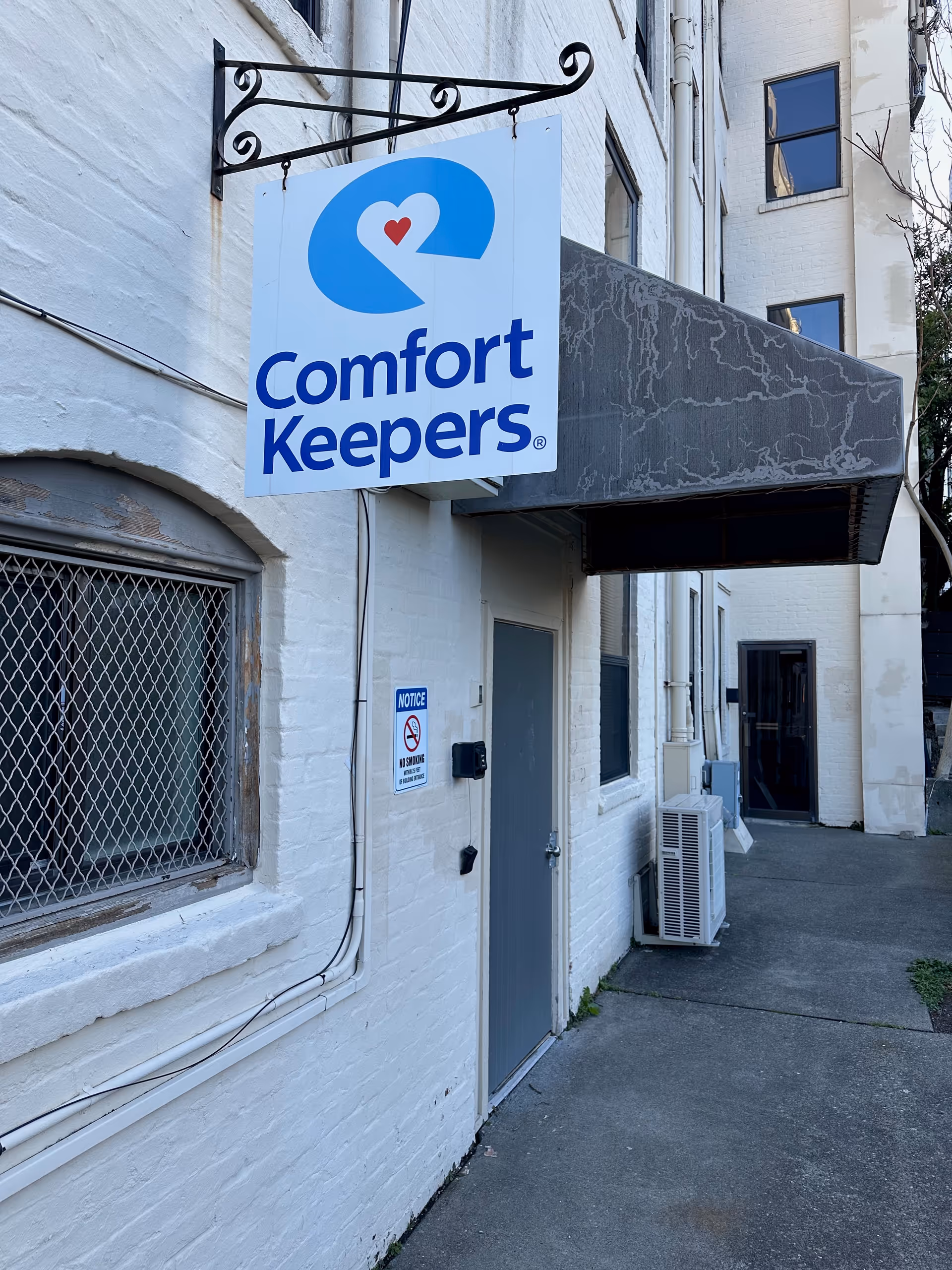 White brick building with Comfort Keepers sign and metal awning along walkway.