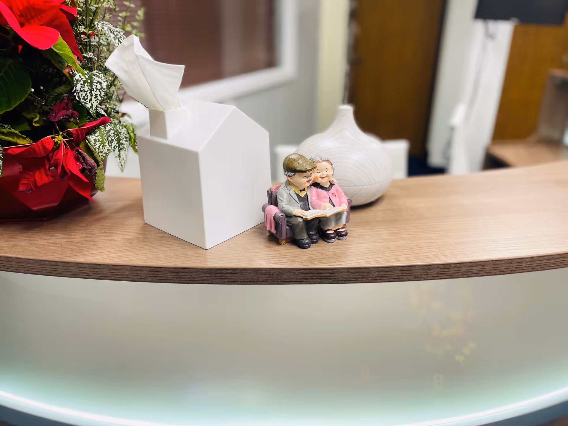 Reception desk with tissue box, small figurines, and a red plant arrangement on a wooden surface.