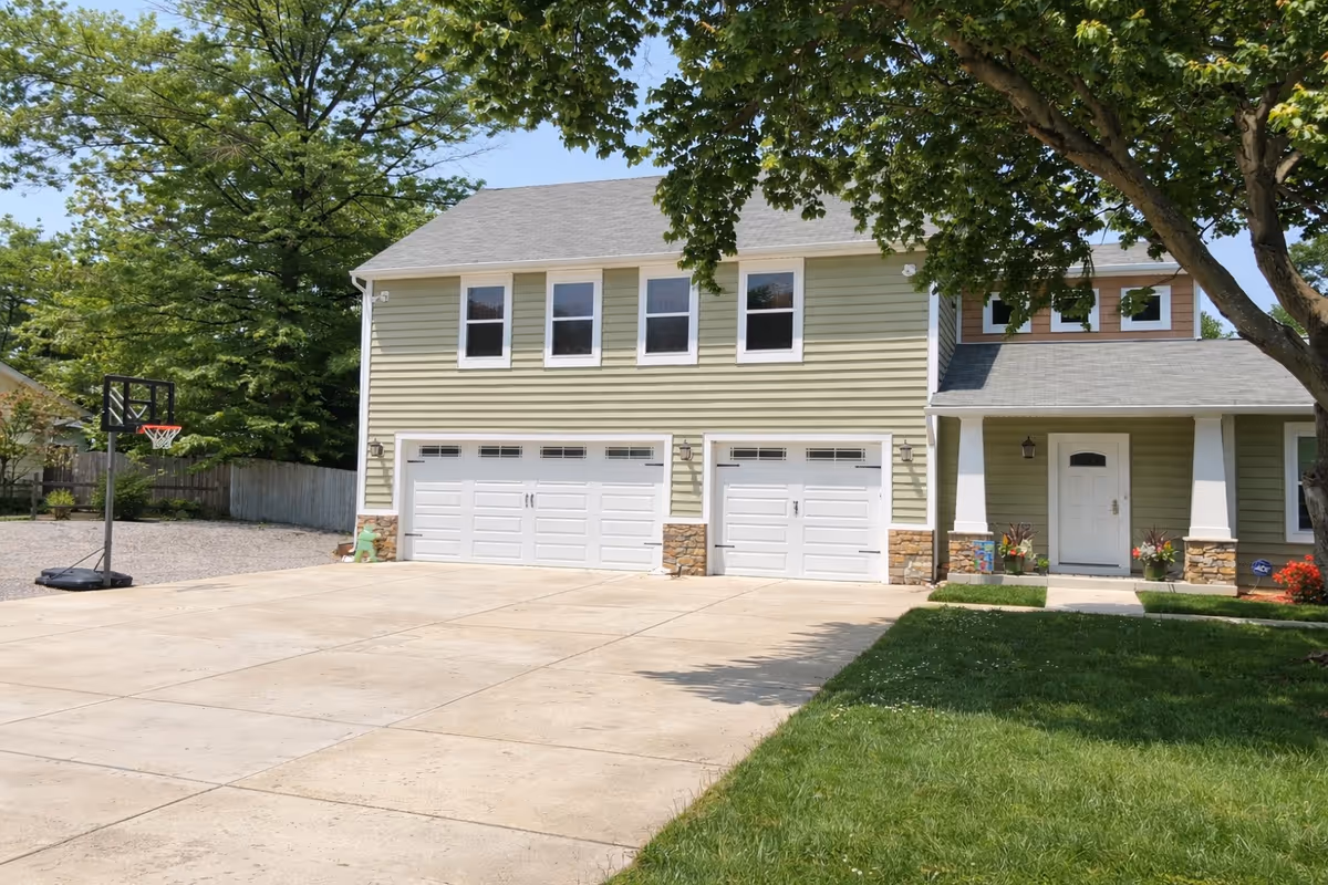 Two-story building with three garage bays, a front porch, and large trees in the yard.