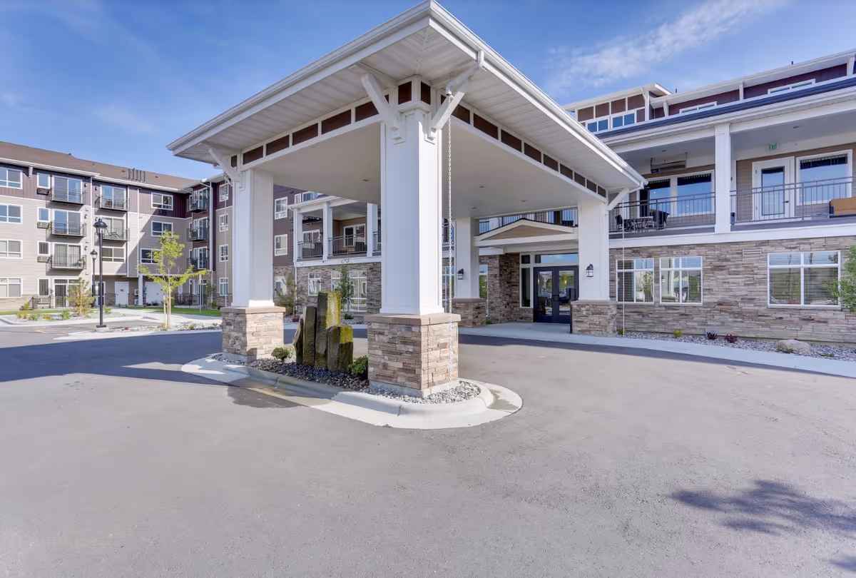A modern senior living building exterior with a covered porte-cochere entry and stone accents.