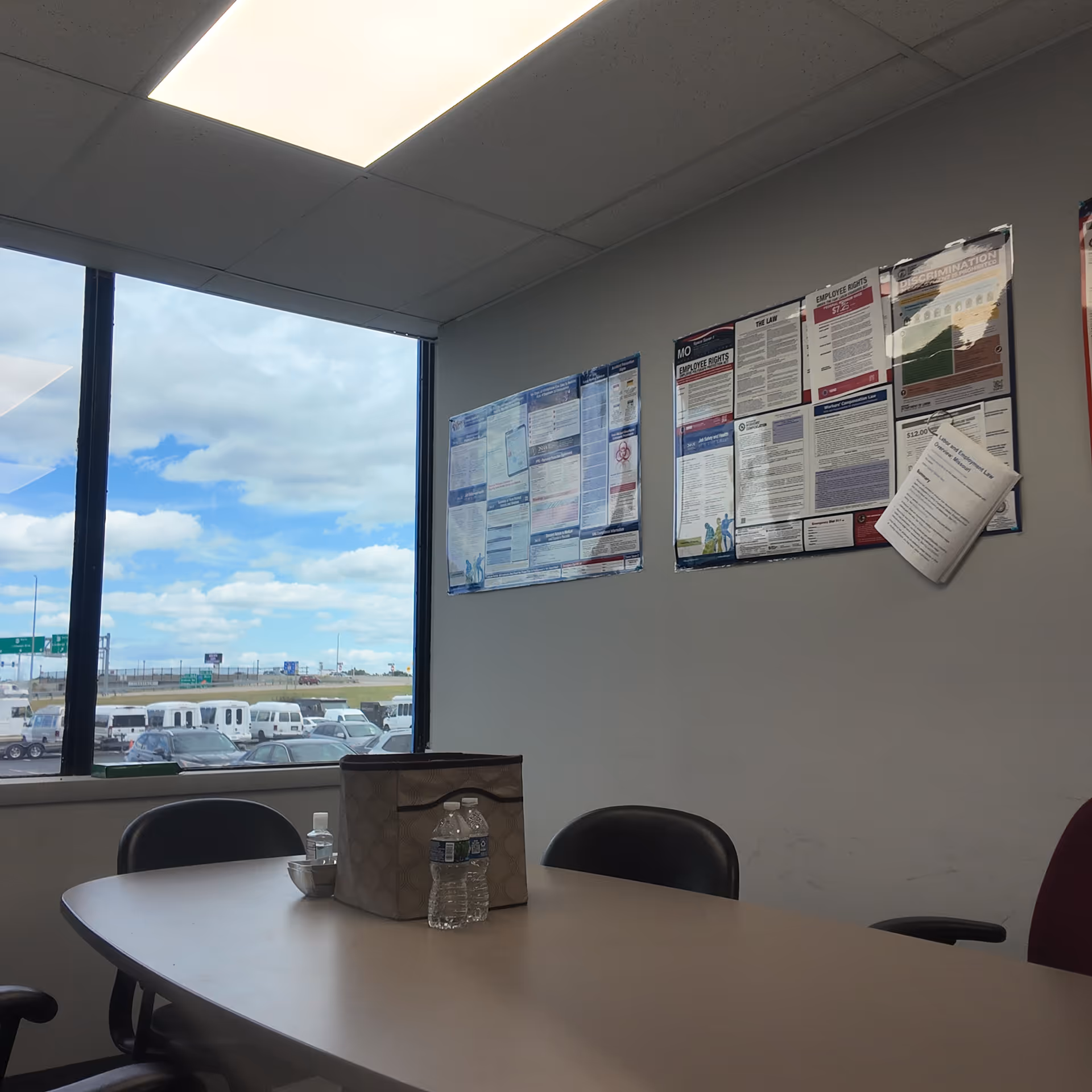 Interior meeting room with bulletin boards, a table, water bottle, and outside parking visible.