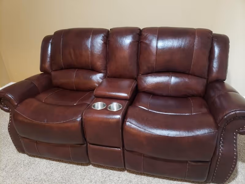 Dark brown leather reclining sofa with cup holders in a carpeted living room.