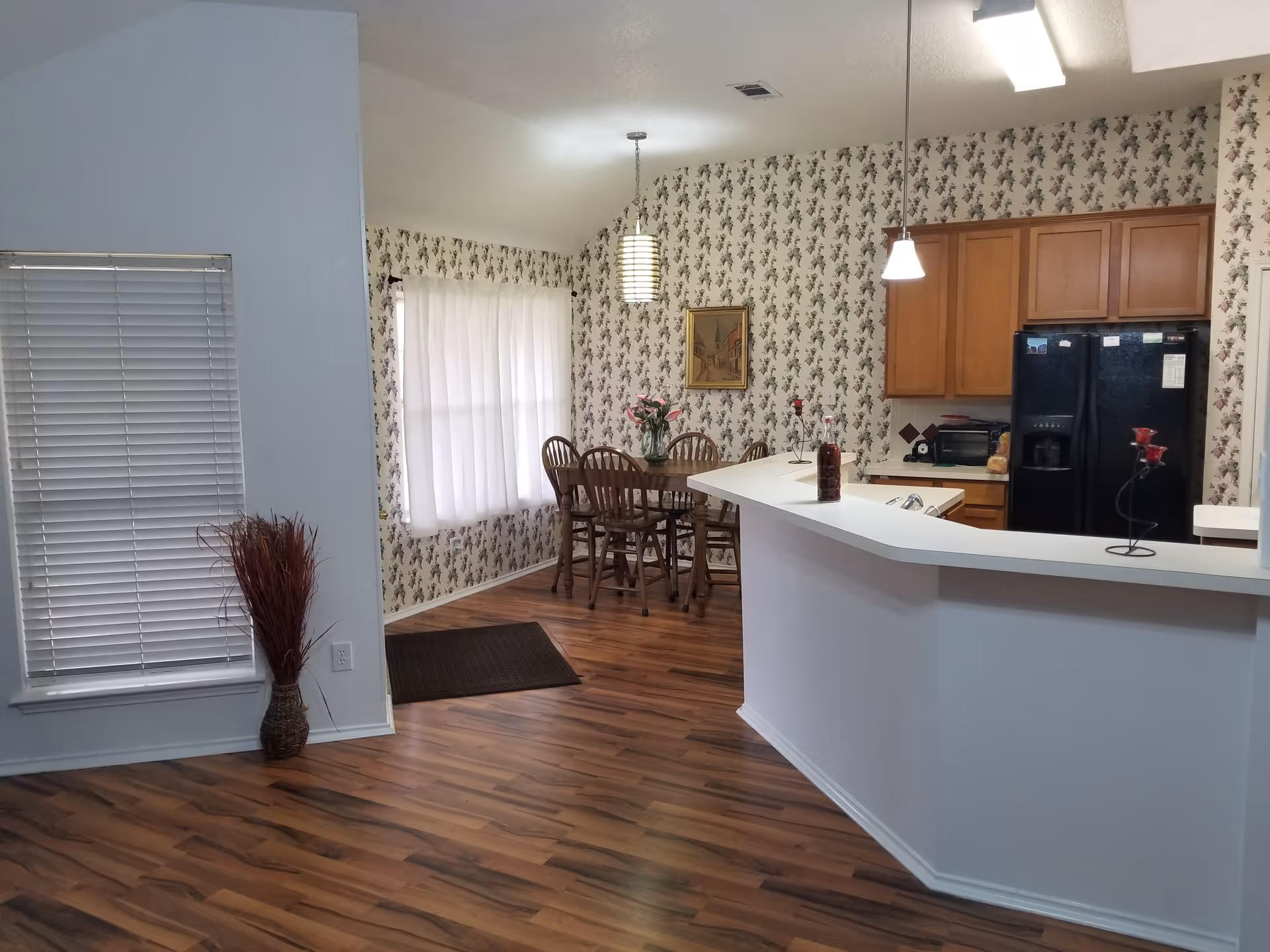 Open-plan kitchen and dining area with island, wooden floor, and floral wallpaper.