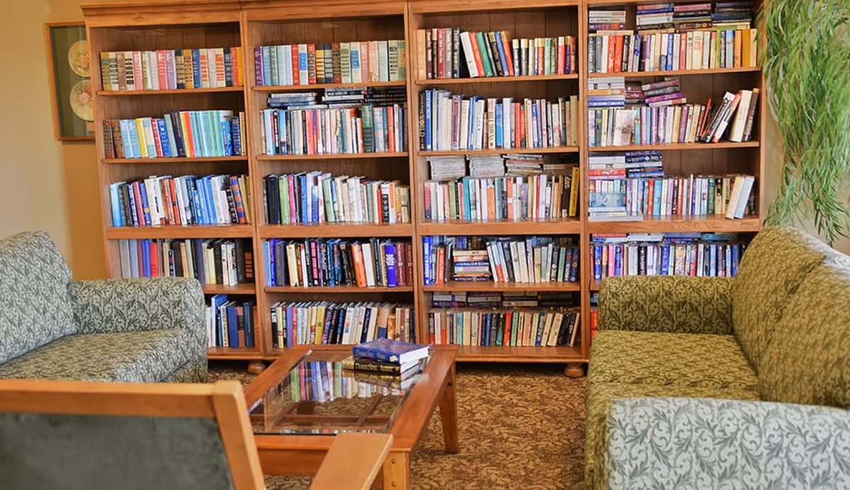 Cozy interior lounge area with large bookshelves, upholstered chairs, and a glass coffee table.