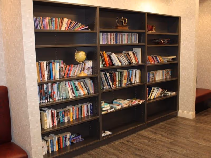A large dark wood bookshelf filled with books and a globe against a patterned wall in a common area.
