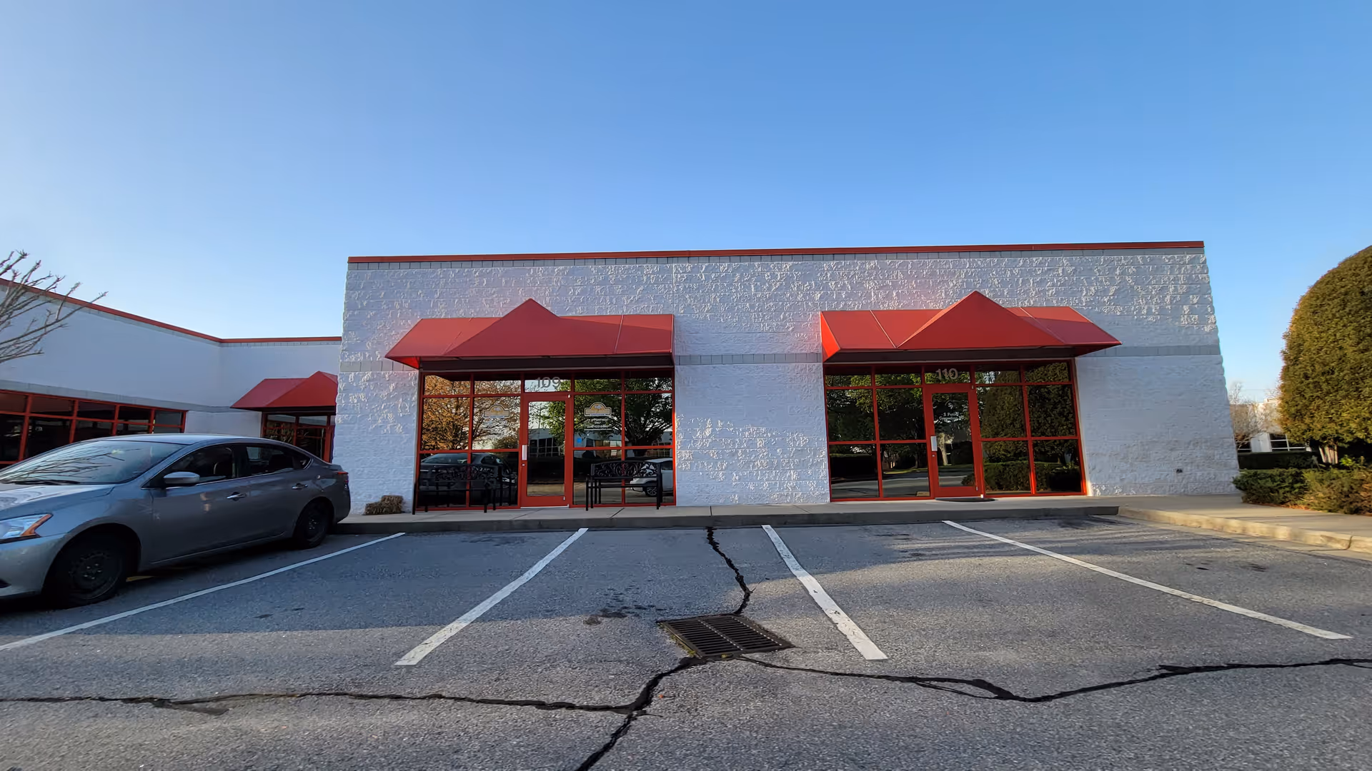 Exterior front of a white building with red awnings and a parking lot.
