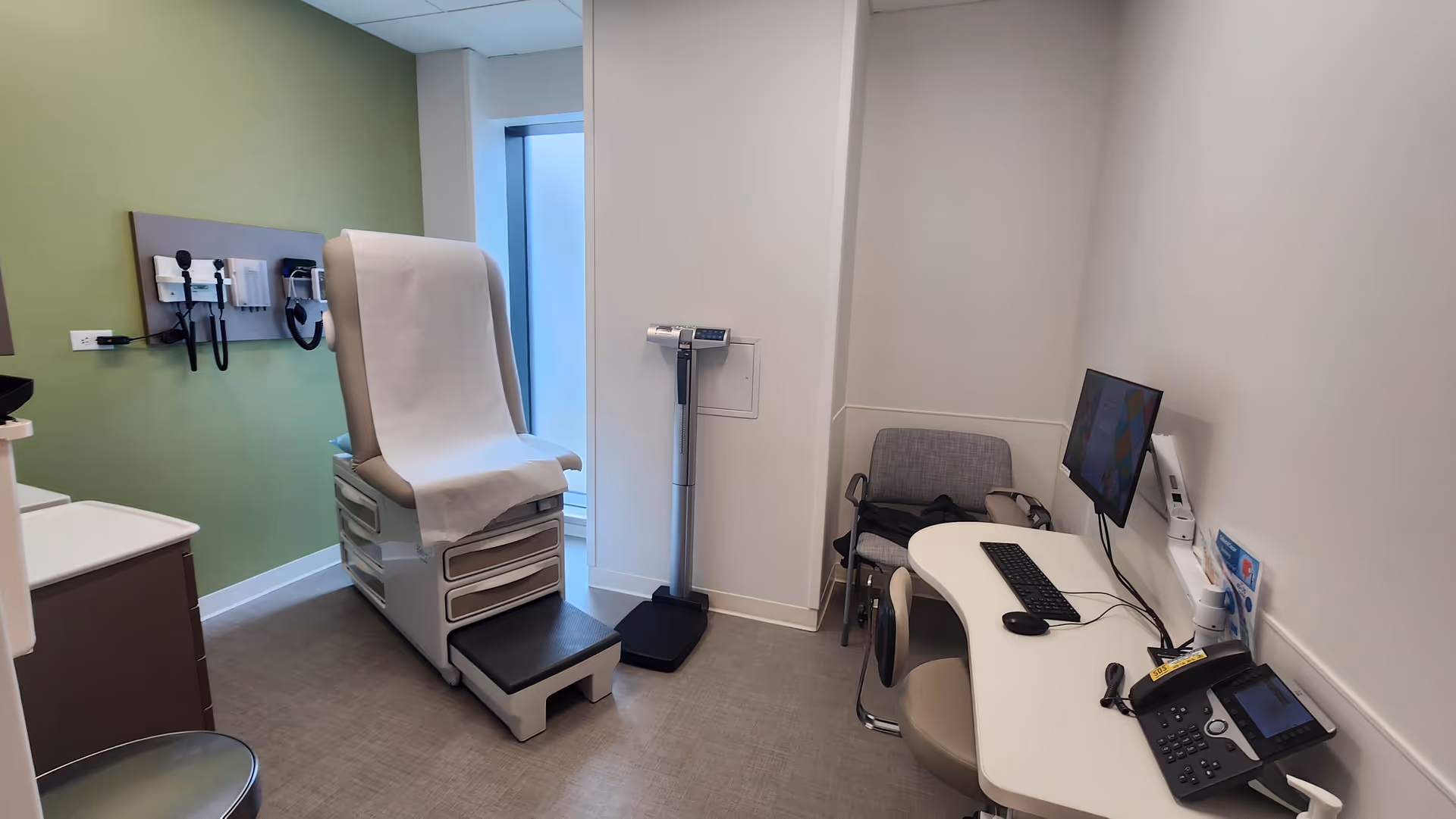Exam chair, medical equipment, and a desk in a clean clinical examination room.