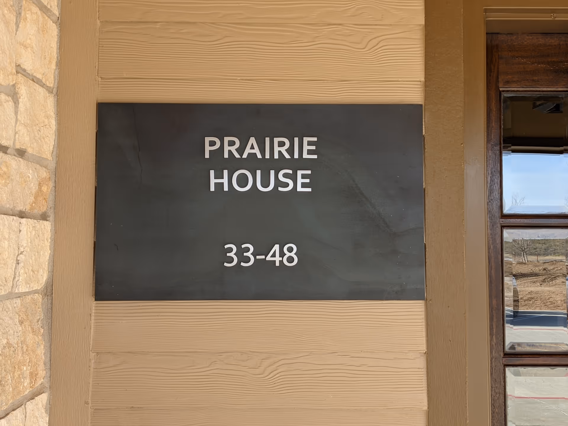 Beige exterior wall with a sign reading PRAIRIE HOUSE 33-48 beside a wooden door.
