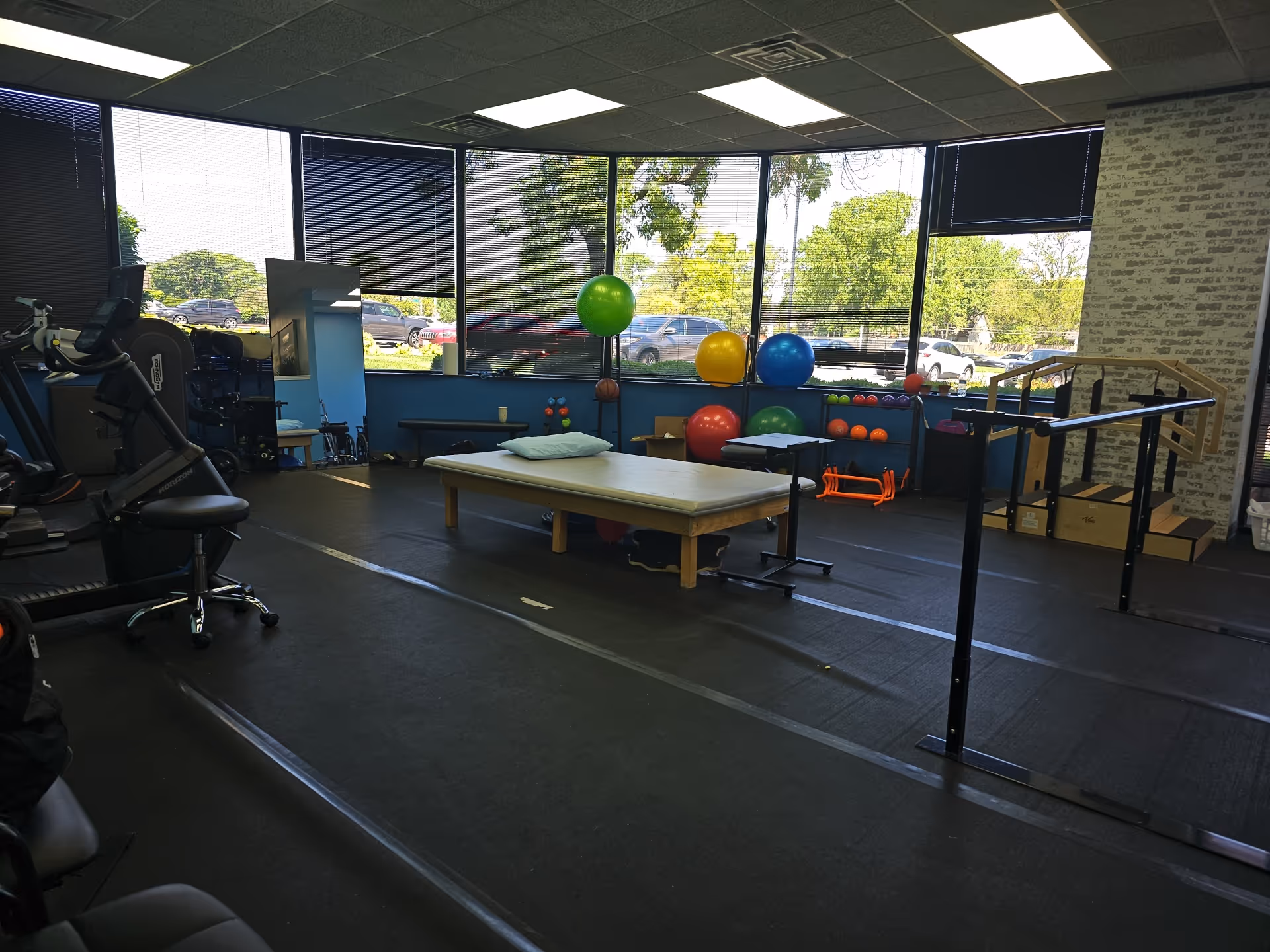 Interior rehab gym with therapy equipment, exercise balls, mats, and parallel bars.