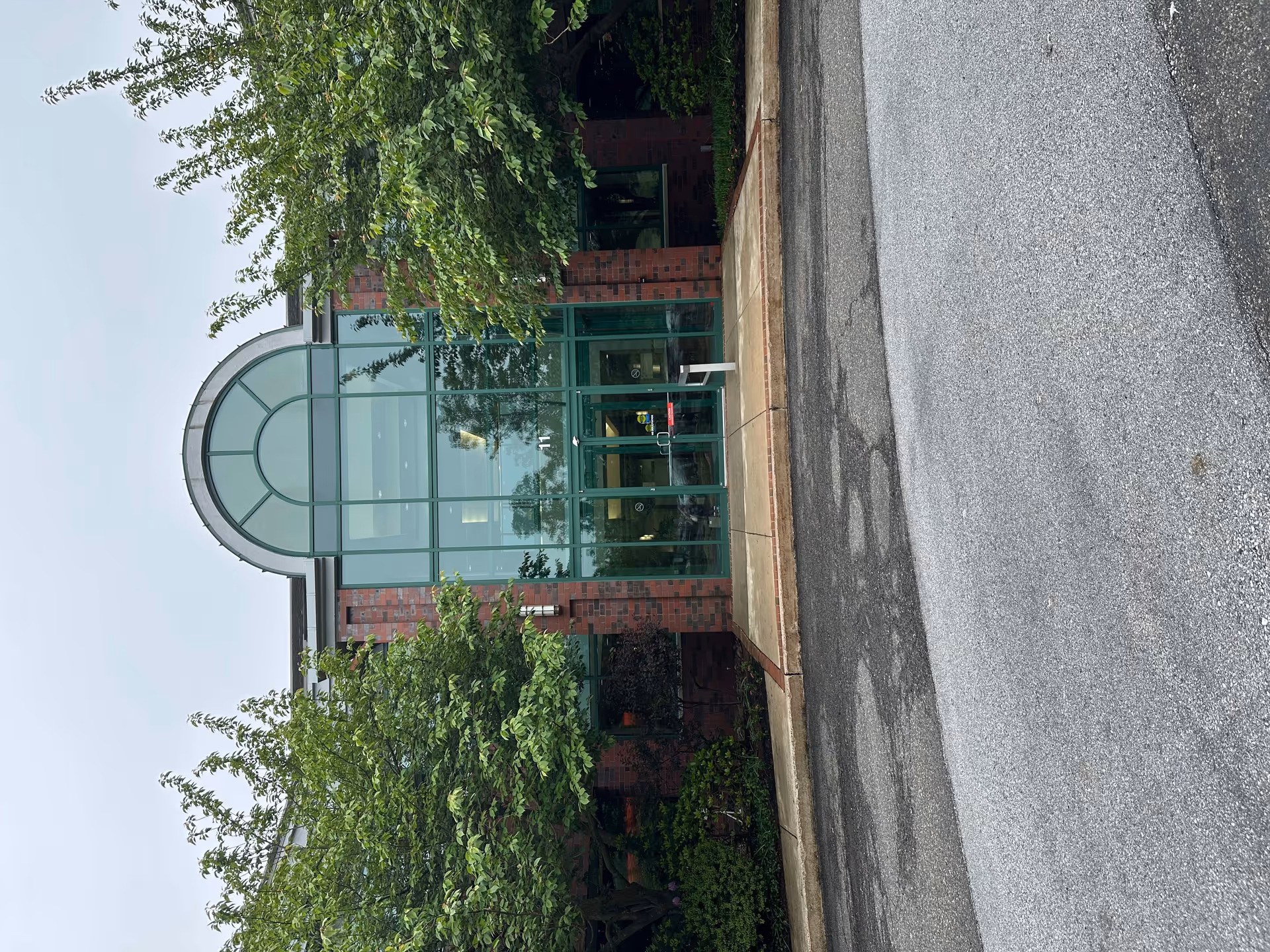 Brick facility entrance with an arched glass facade and surrounding greenery.