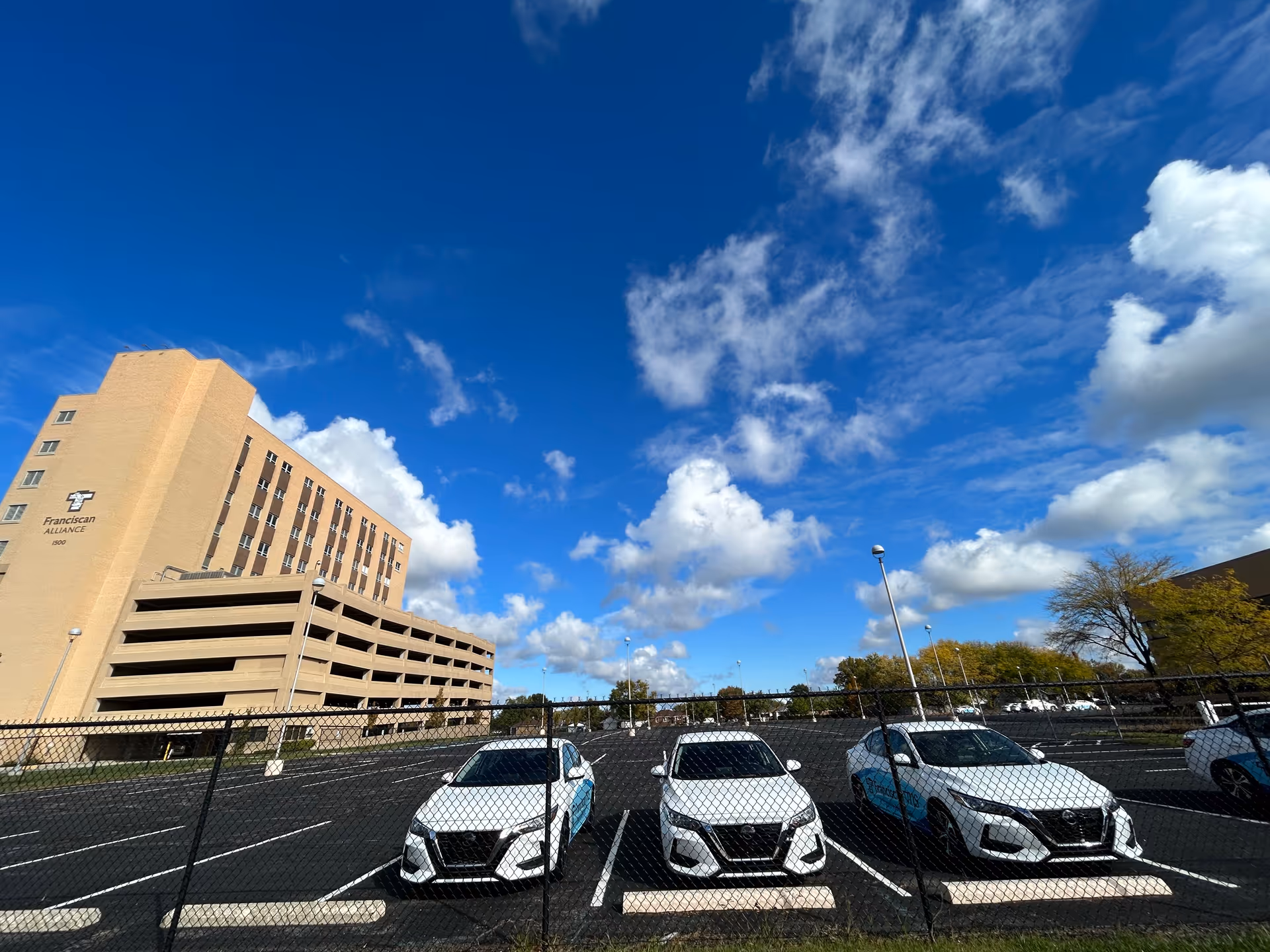 Exterior view of a Franciscan Alliance building with a fenced parking lot and cars.