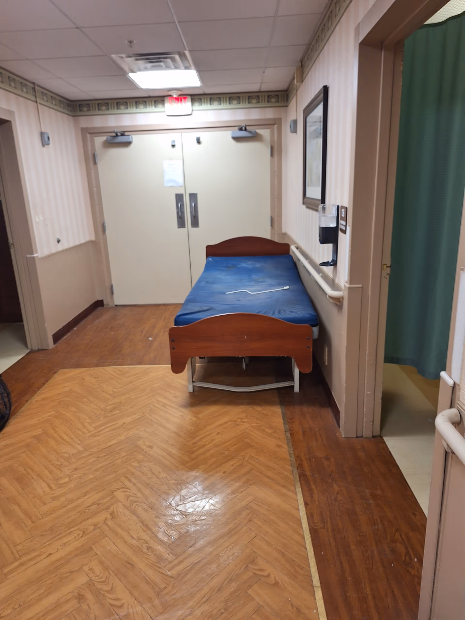 Hospital-style hallway with a blue bed placed near double doors.