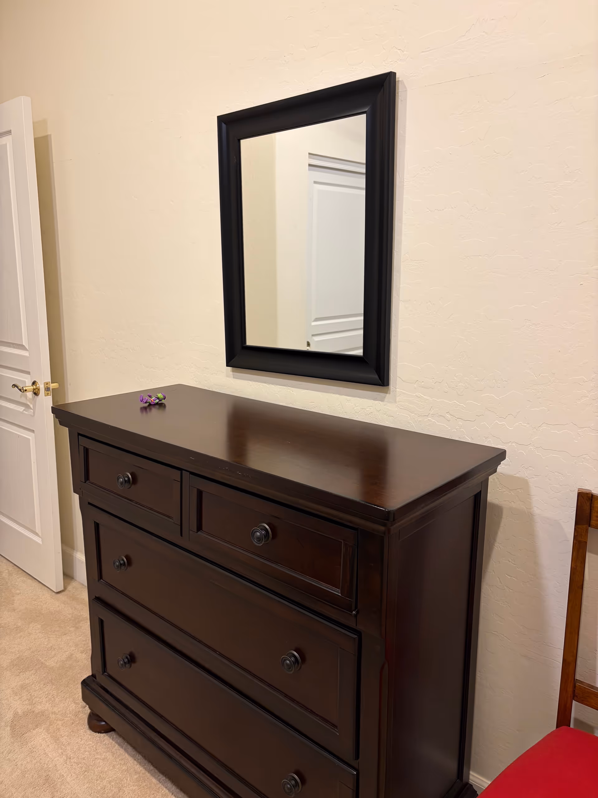 Dark wood dresser with a rectangular framed mirror on a light textured wall.