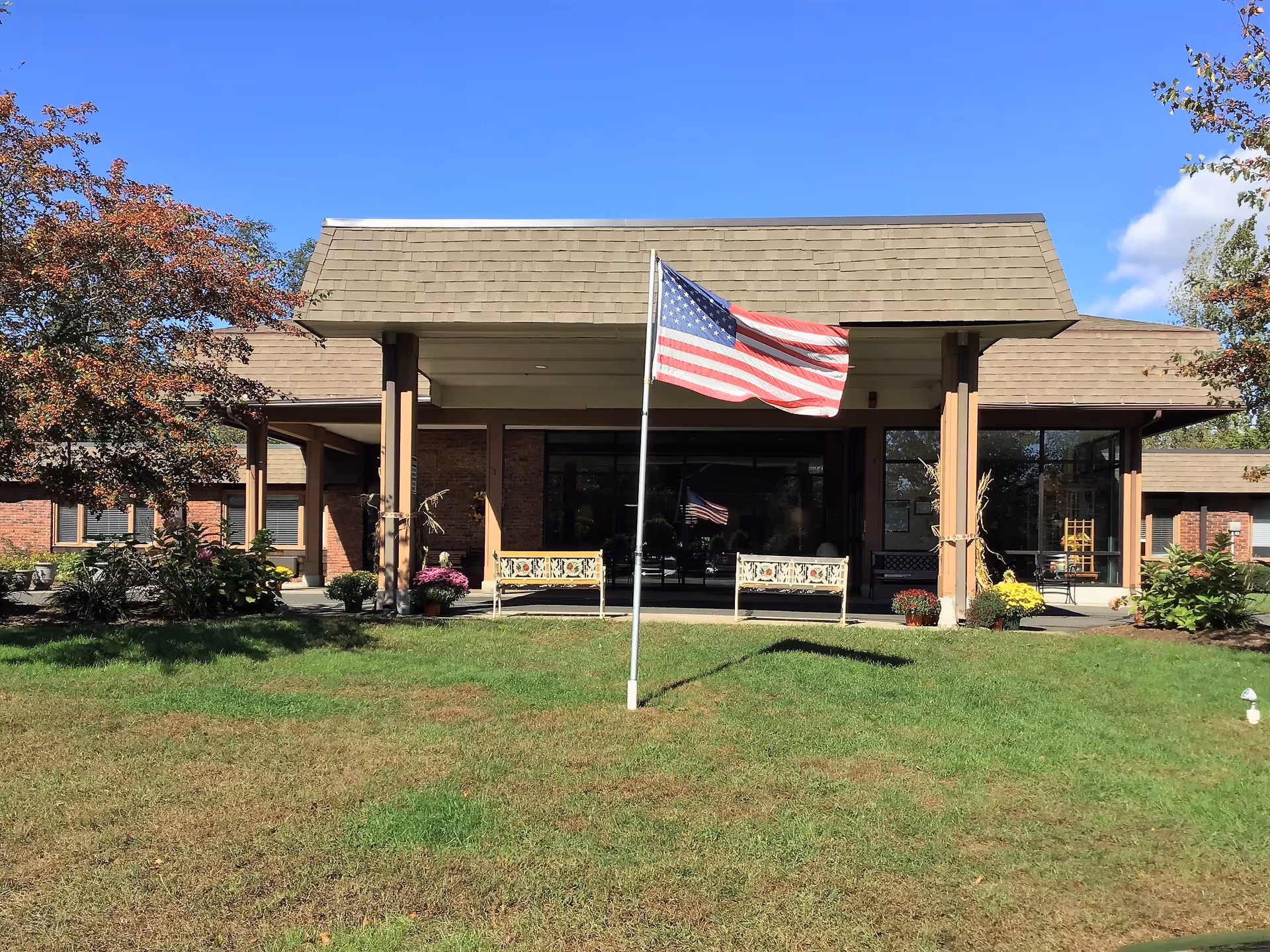 Front view of Parkway Pavilion Health and Rehabilitation Center with American flag and benches.