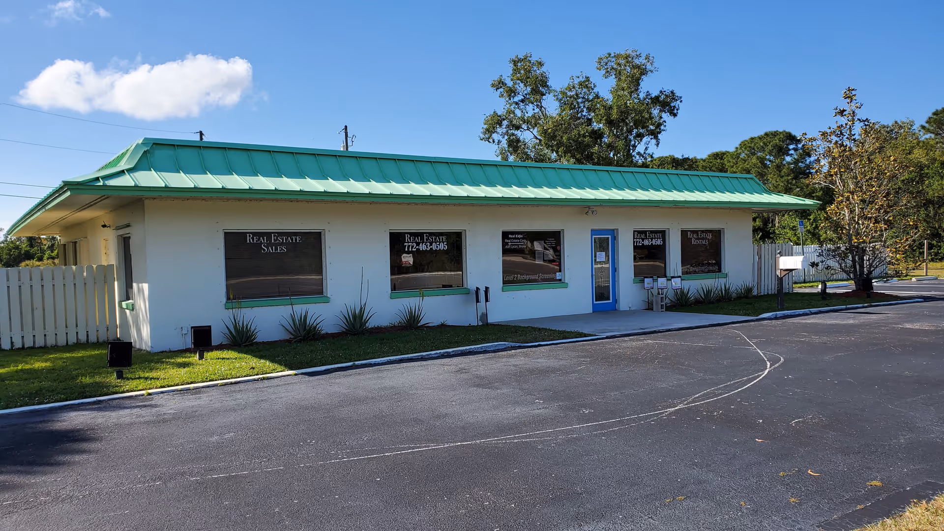 Front exterior of a single-story building with a green metal roof, white walls, and blue door.