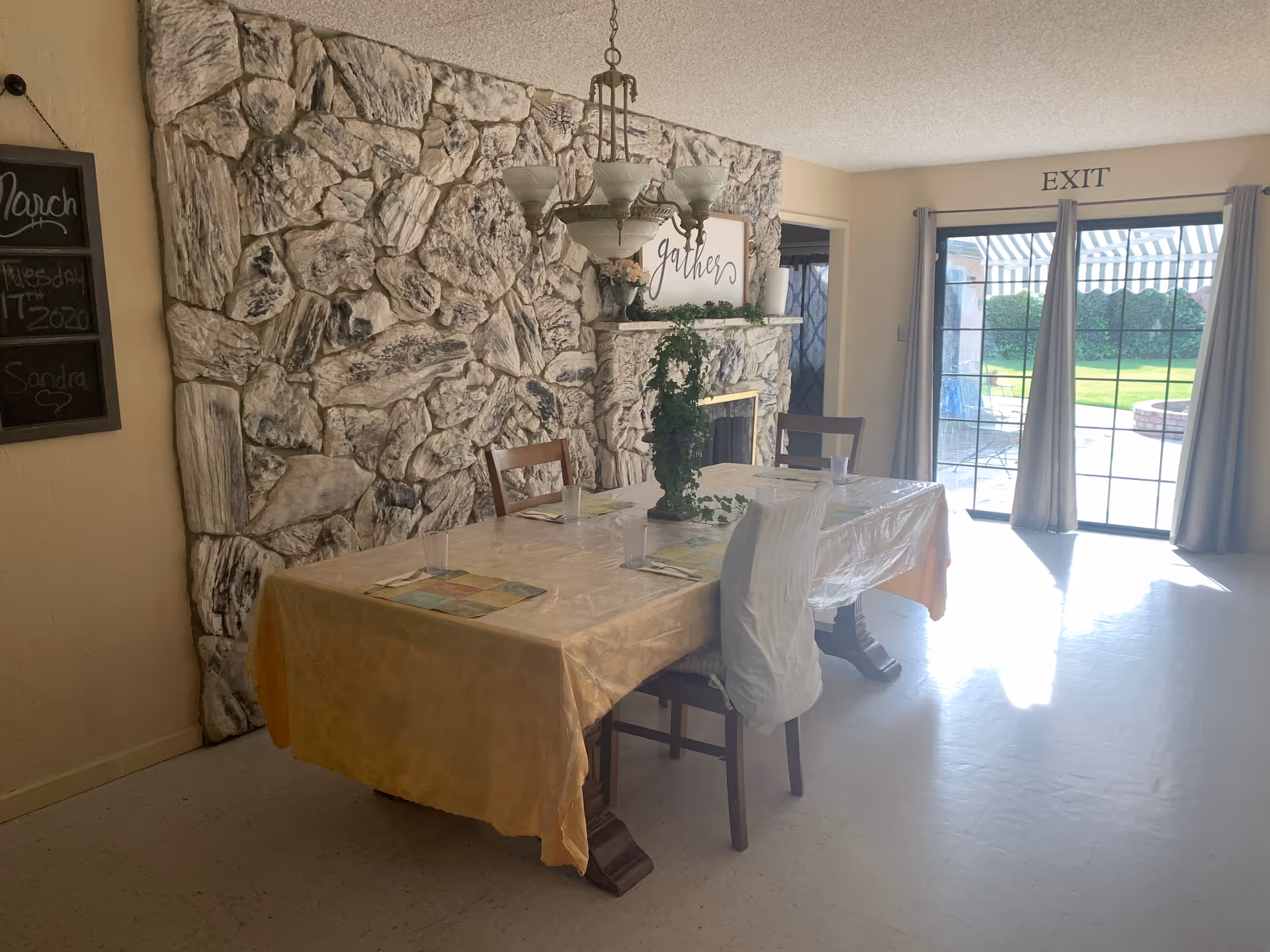Dining room with a stone fireplace wall, long table set for a meal near exit doors.