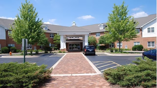 Brick senior living facility entrance with a brick-paved walkway and trees.