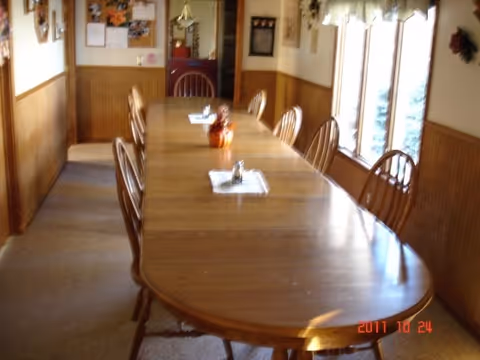 A long wooden dining table with chairs in a cozy senior living facility dining room.