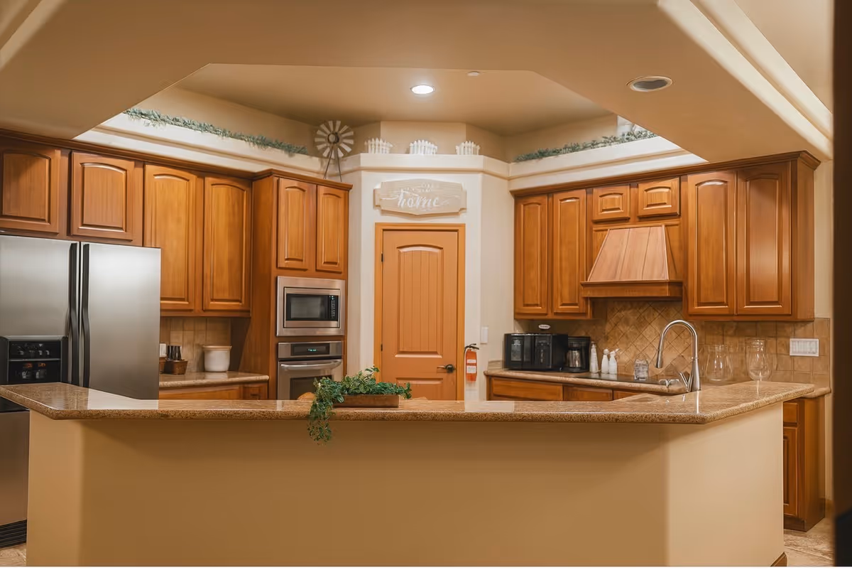 Warm kitchen in a senior living facility with wooden cabinets, island, and stainless appliances.