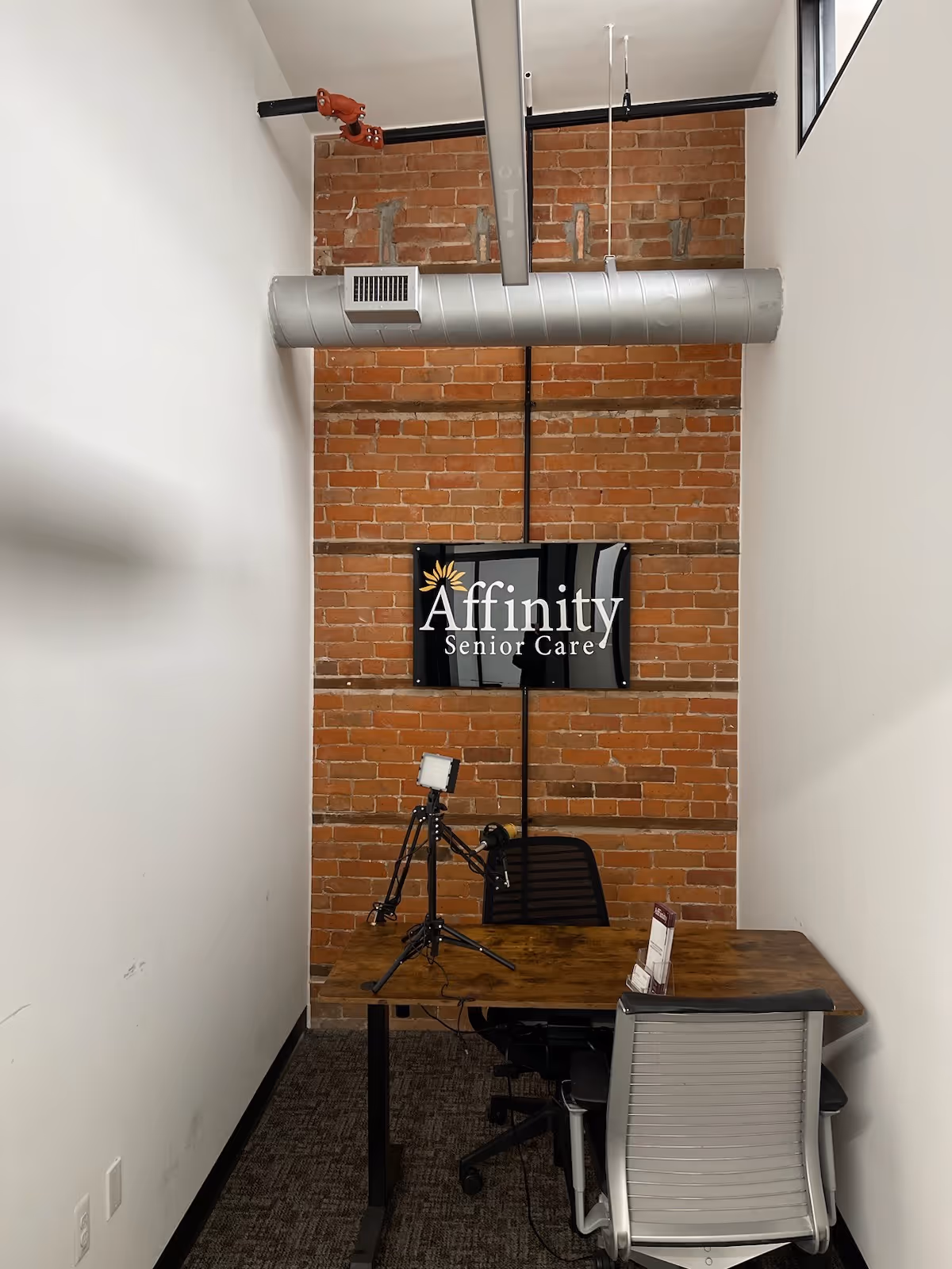 Interior office/studio corner at Affinity Senior Care with brick wall, sign, desk and filming gear.