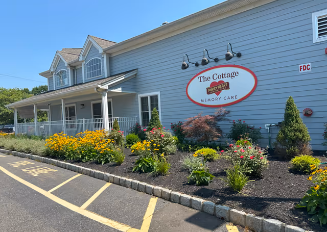 Blue senior living facility exterior with a landscaped garden and sign reading Merry Heart Memory Care.