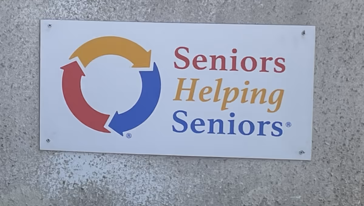 Outdoor wall sign reading 'Seniors Helping Seniors' with circular colored arrows