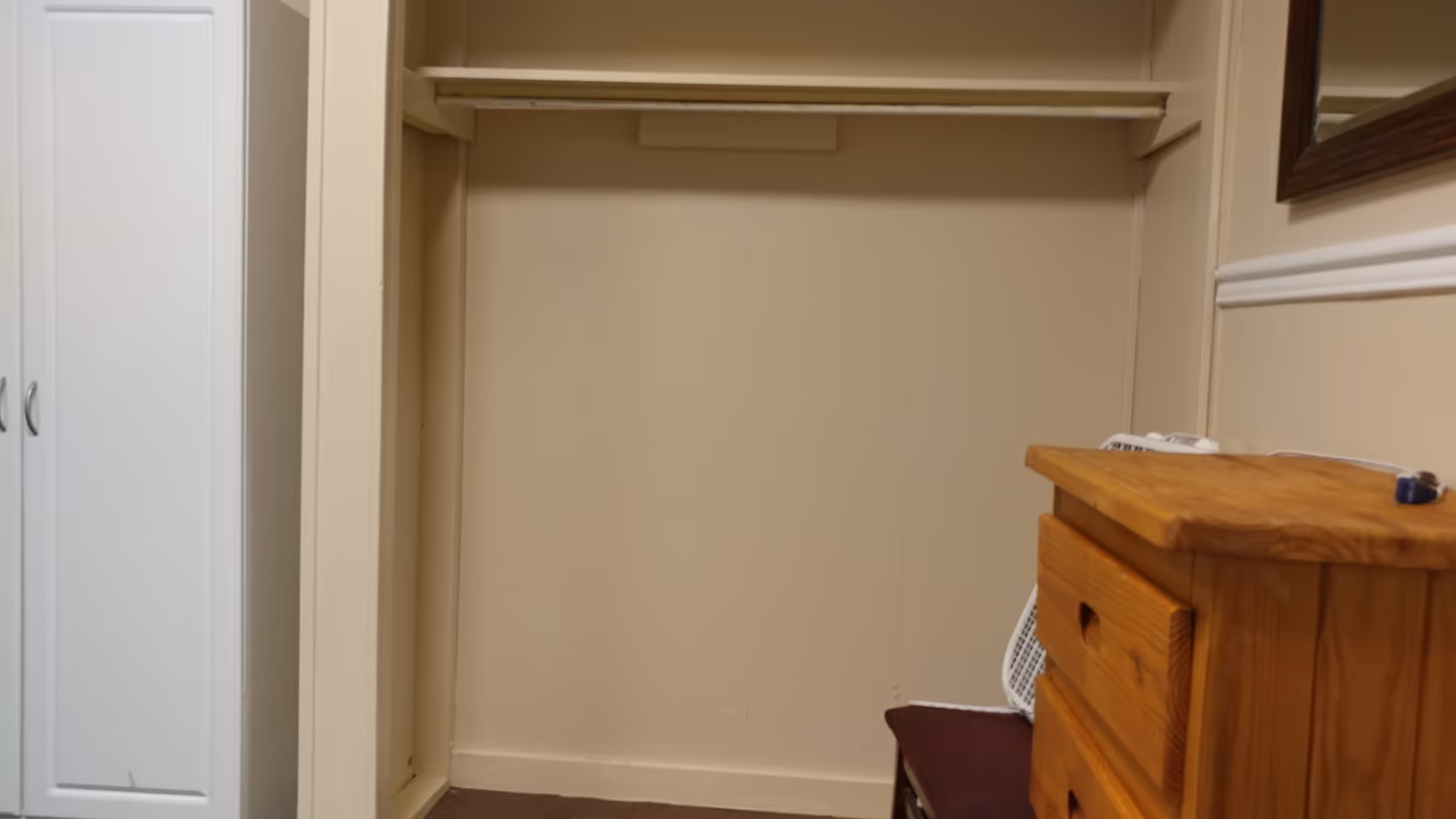 Small interior closet with a hanging rod, shelves, and a wooden dresser.