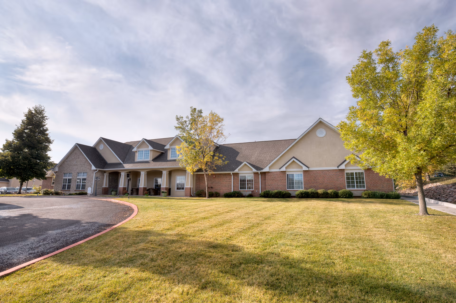 Front exterior of a Brookdale Broadmoor senior living building with lawn and trees.