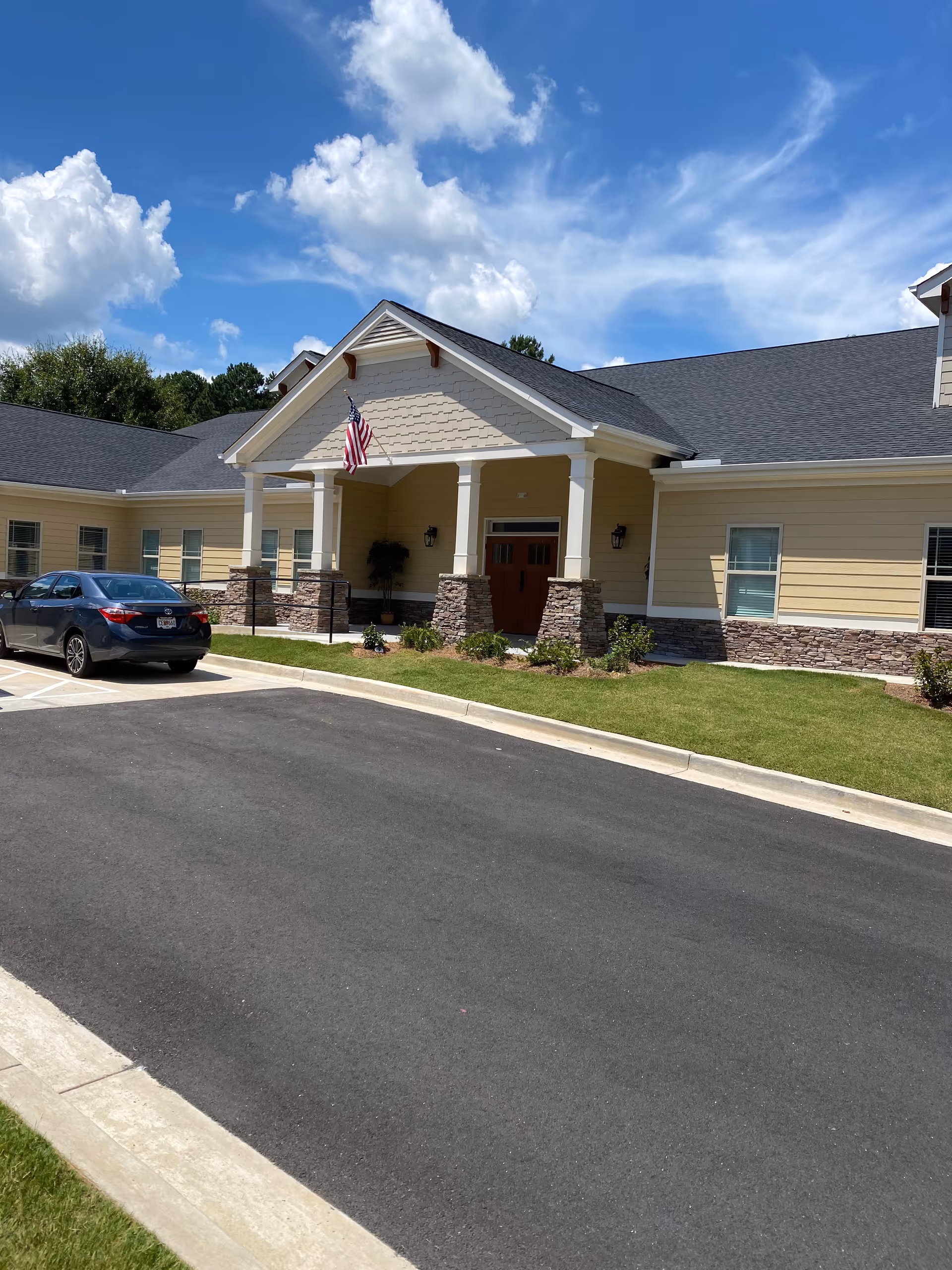 Front view of a beige senior care home with stone pillars, gable roof, and parked car.