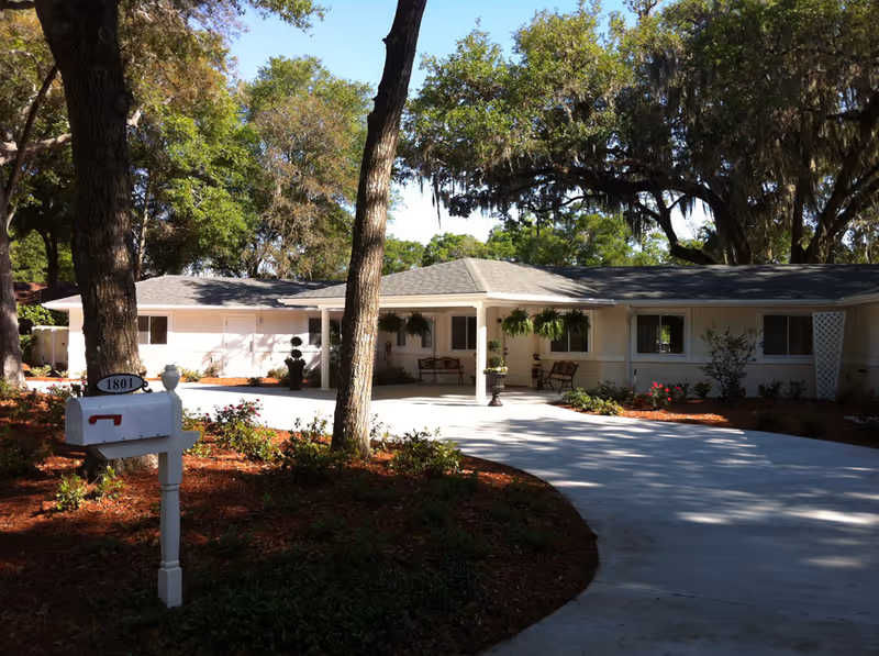 Oak Village senior living facility exterior with driveway, benches, and trees.
