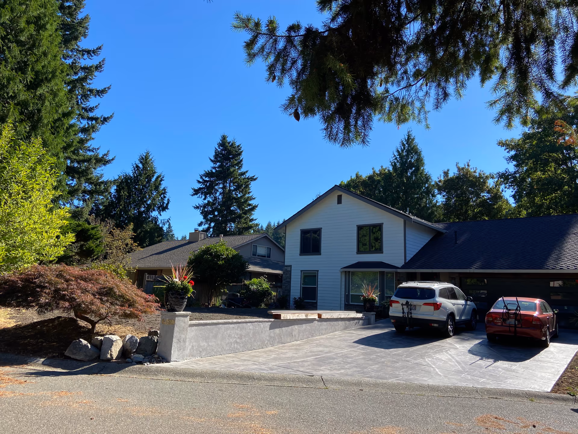 A senior living home with a driveway, parked cars, and surrounding trees under a blue sky.