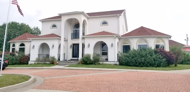Two story white senior living facility with arched entryways and manicured landscaping.