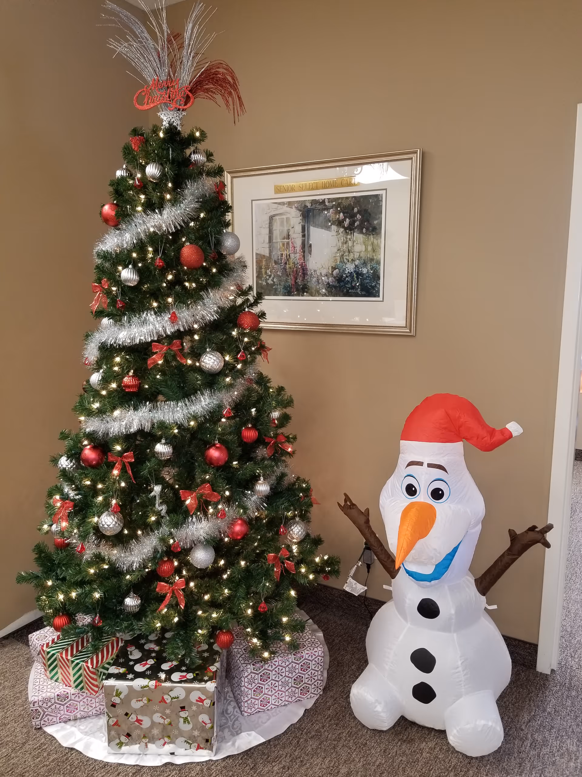 A decorated Christmas tree with wrapped gifts and a large inflatable snowman in a beige room.